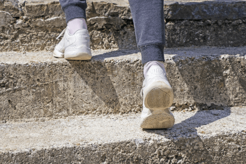 Detailaufnahme von Beinen in Sportschuhen, die eine Steintreppe nach oben steigen – Symbol für proaktive Bewegung und Entwicklung.